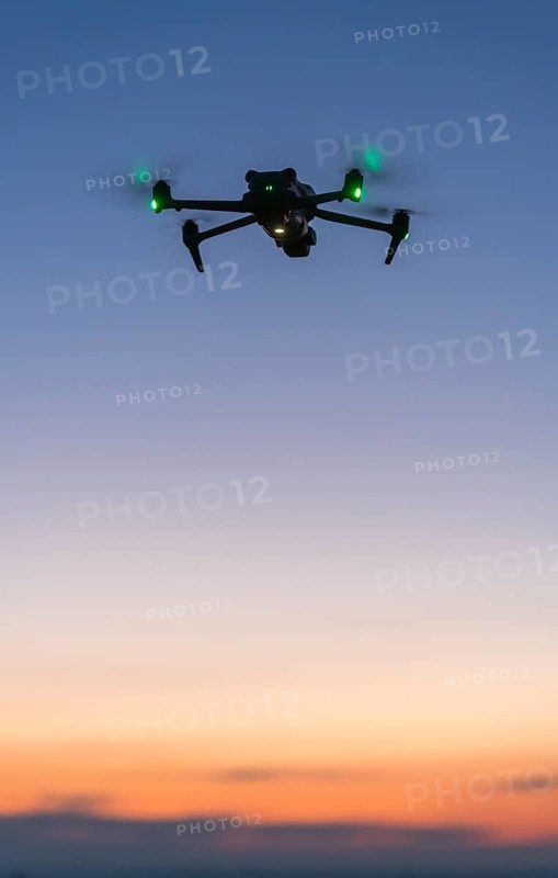 Drone floats in soft evening sky with green lights