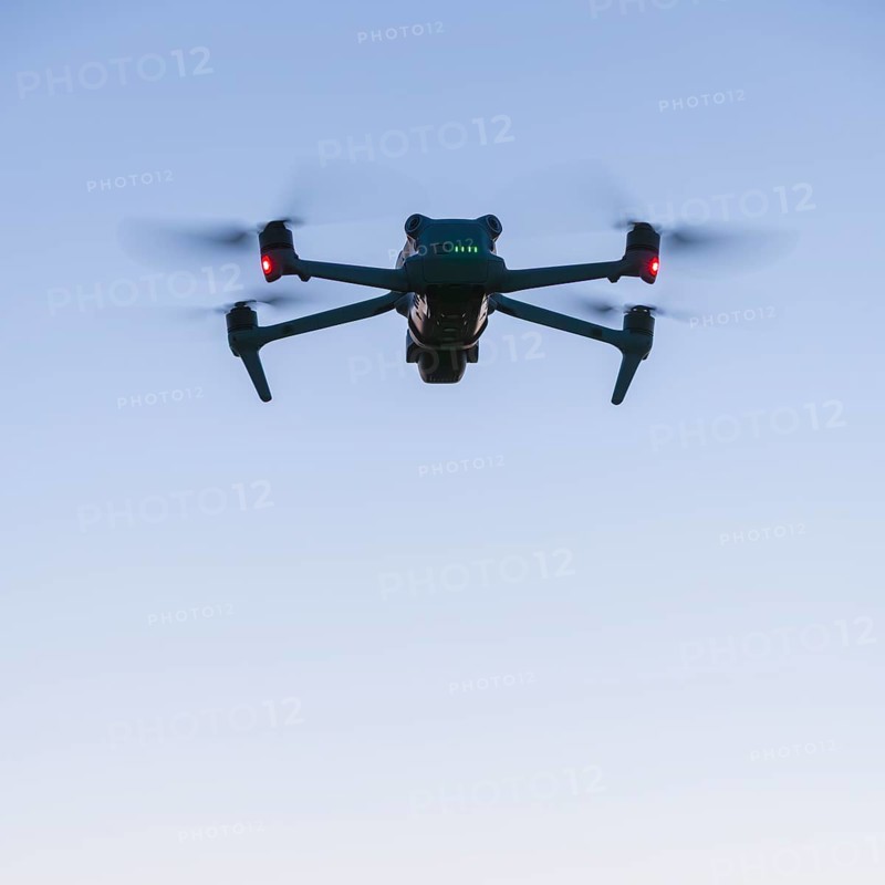 Drone with illuminated propellers floats against the evening sky