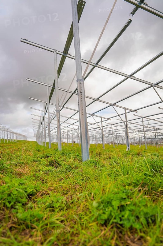 Close-up of metallic solar frames in the construction phase on a green field under cloudy sky, Energiewende, construction of PV open space, Baden-Württemberg, Germany