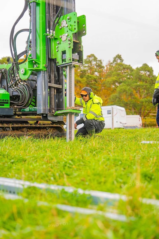A worker kneels next to a drilling rig in a meadow and adjusts the machine, Energiewende, construction of PV open space, Baden-Württemberg, Germany