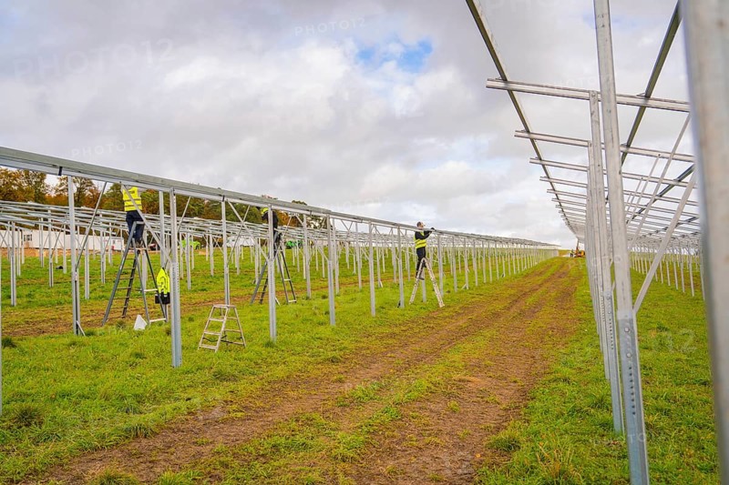 Workers assemble metal structures on a construction site in a grassy field, Energiewende, construction of PV open space, Baden-Württemberg, Germany