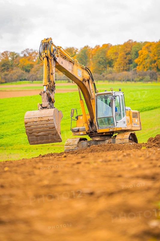 Excavator lifts soil in a green landscape with autumn trees, energy revolution, construction of PV open space, Baden-Württemberg, Germany