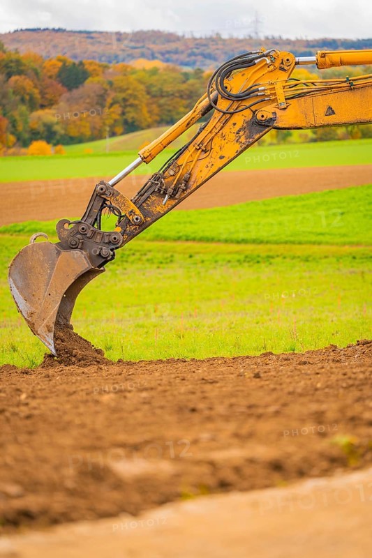 Close-up of an excavator bucket moving earth surrounded by green fields, energy transition, construction of PV open space, Baden-Württemberg, Germany