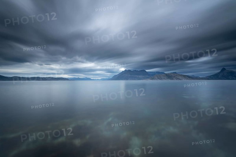 The Vestfjord in Nordland, Norway, near Bodø, impresses with a dramatic atmosphere. Dark clouds sweep across the water and create a mystical atmosphere. The rugged cliffs and majestic mountains are reflected in the tranquil fjord and provide an impressive backdrop