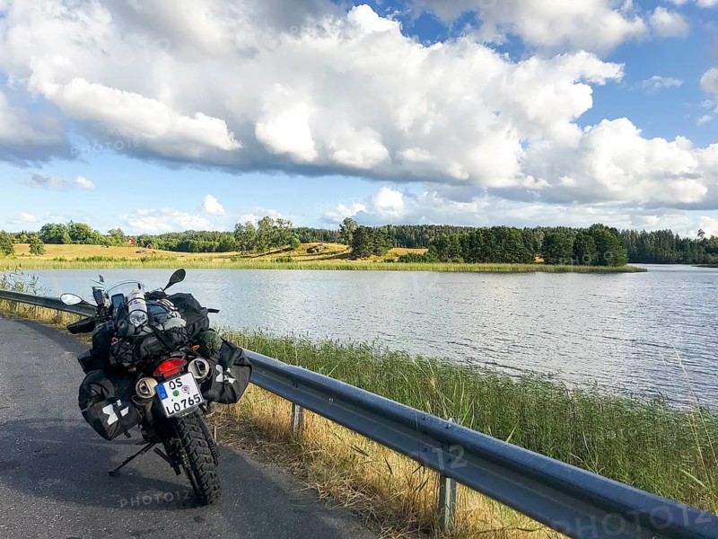 A BMW Sertao Enduro G650GS motorcycle stands on a road next to a lake under a cloudy sky surrounded by green nature, Sparreholm, Södermanslän, Sweden