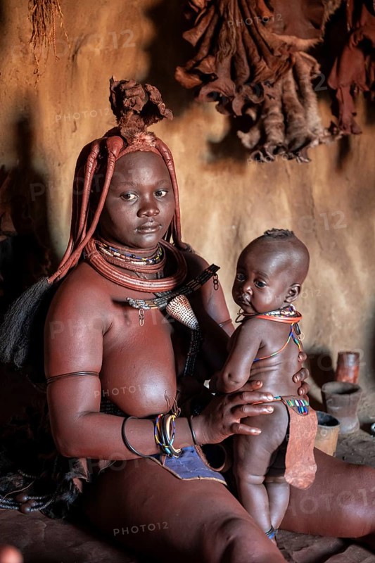 Himba woman sitting with baby in traditional hut, Himba village, Kaokoveld, Kunene, Namibia