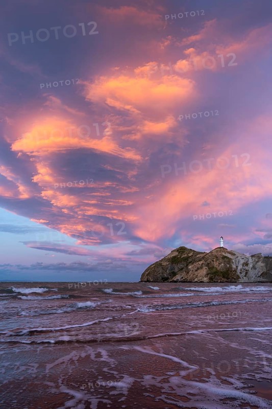 Castlepoint Beach, ocean and lighthouse on a rock, evening, sunset, dramatic sky. Castlepoint, Wairarapa Coast, Wellington Region, North Island, New Zealand