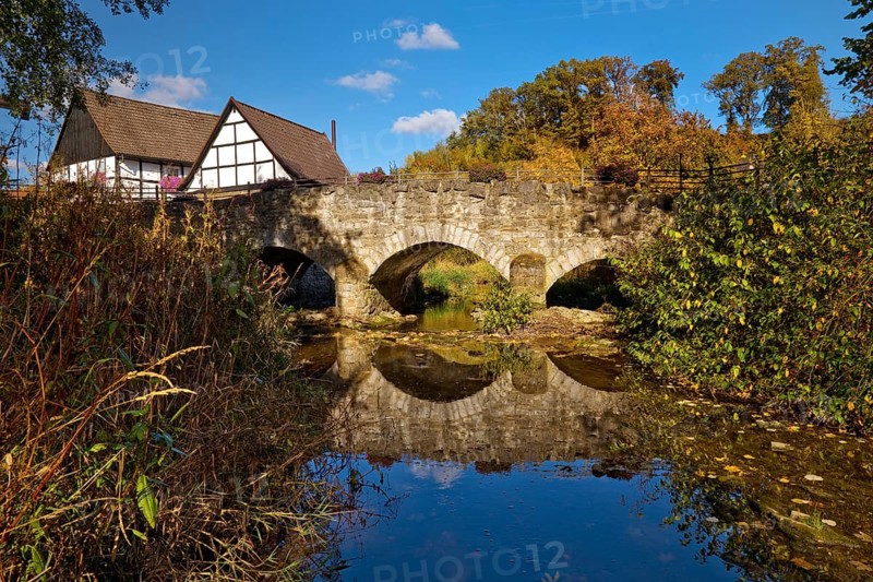 The river Hönne with the old Hönnetalbrücke in autumn with half-timbered house in Volkringhausen, Balve, Sauerland, North Rhine-Westphalia, Germany