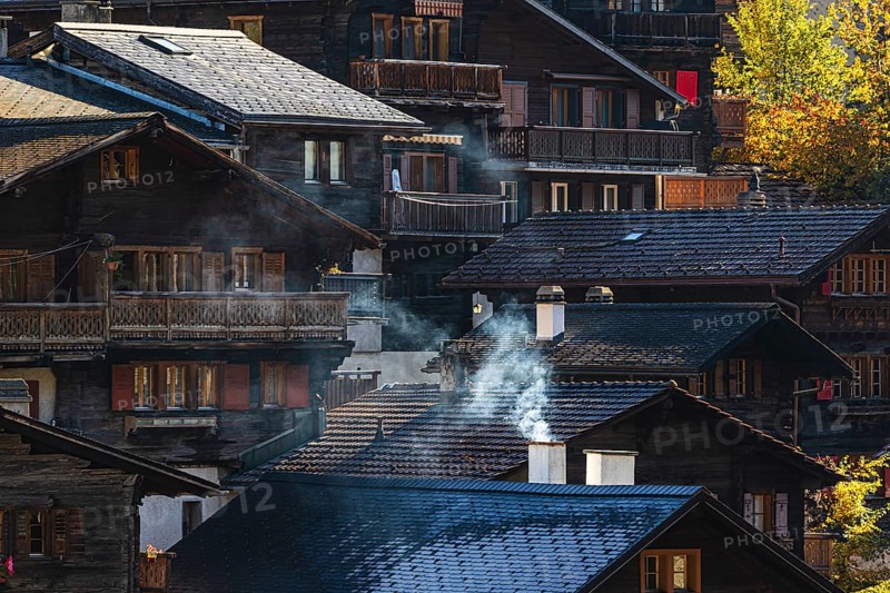 Smoke rises over the roofs of old wooden houses in Vissoie, Val d'Anniviers, Valais Alps, Canton of Valais, Switzerland