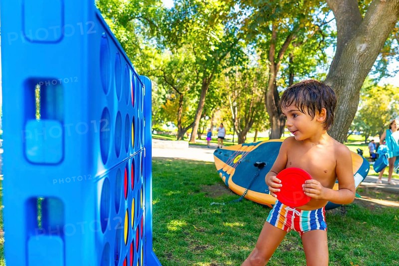 Young boy concentrating on playing a giant connect four game in a park on a summer day, holding a red disc and getting ready to drop it into the grid