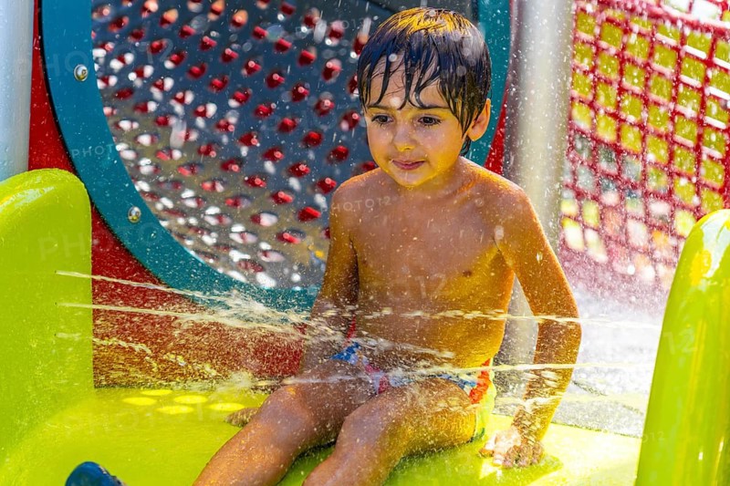 Young boy is having fun playing and splashing in the water jets at a colorful splash park in kamloops, british columbia, enjoying a refreshing summer day outdoors