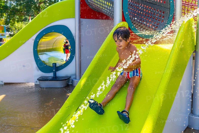 Happy child enjoying a sunny summer day, sliding down a bright green water slide at a splash park, getting sprayed with refreshing water in kamloops, british columbia, canada