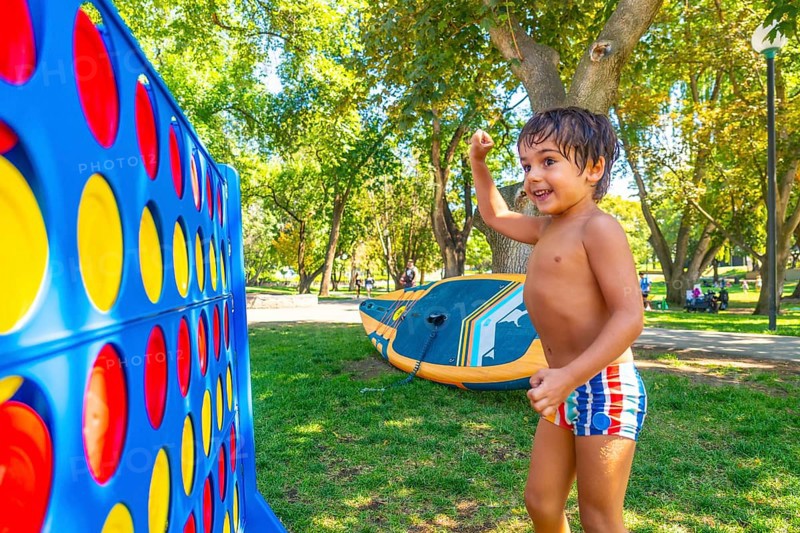Happy child celebrating winning a game of giant four in a row in a park in kamloops, british columbia, with inflatable stand up paddleboard in the background on a sunny summer day