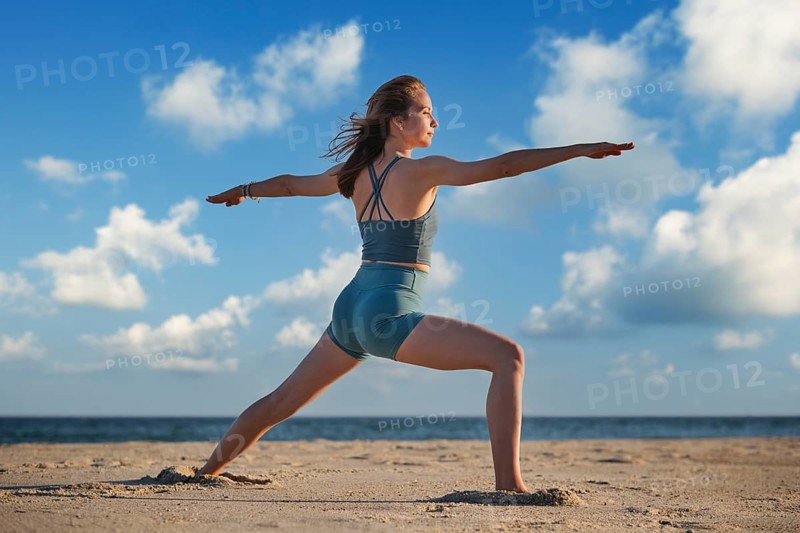 A woman practices Warrior 2 Virabhadrasana 2 pose on the beach during sunset, embodying strength and peace in her yoga practice
