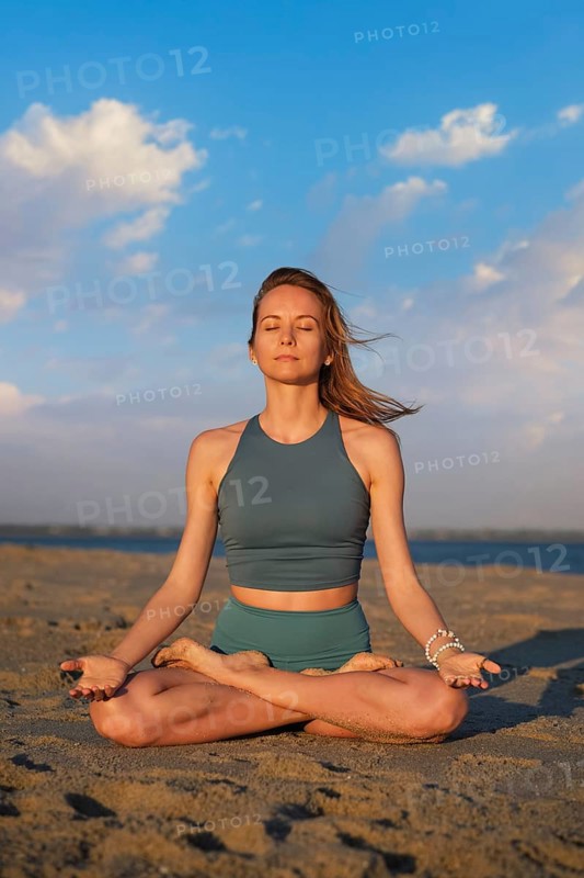 A woman performs Ashtanga Vinyasa yoga in Padmasana with Chin mudra on the beach, meditating peacefully as the sun sets