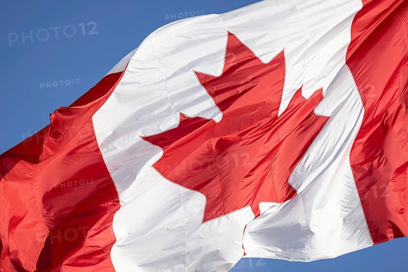 Red and white Canadian flag with a maple leaf waving in the air in downtown Toronto near Ontario Lake. Canadian patriotism and culture