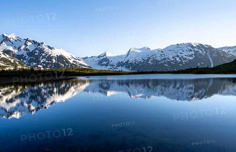 Mountain peaks with Portage Glacier glacier and snow reflected in Divide Lake mountain lake in evening light, Portage Pass Trail, Whittier, Alaska, USA
