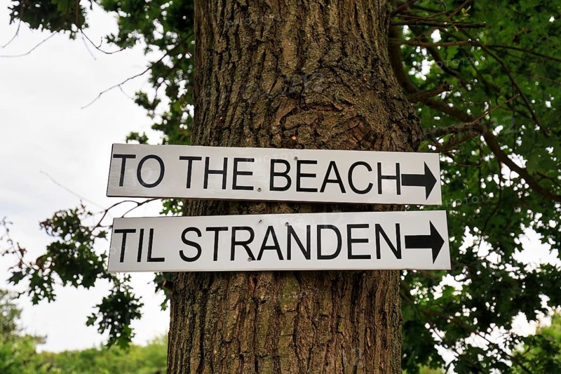 Bilingual signs with inscription, direction sign to the beach on a tree, Galløkken Strand, Rønne, Bornholm, Denmark