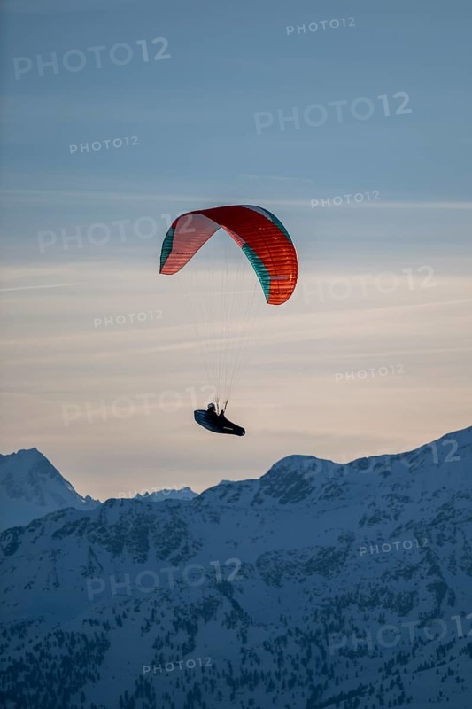 Paragliders flying over snowy mountain peaks in winter in evening light, Kitzbühel Alps, Tyrol, Austria