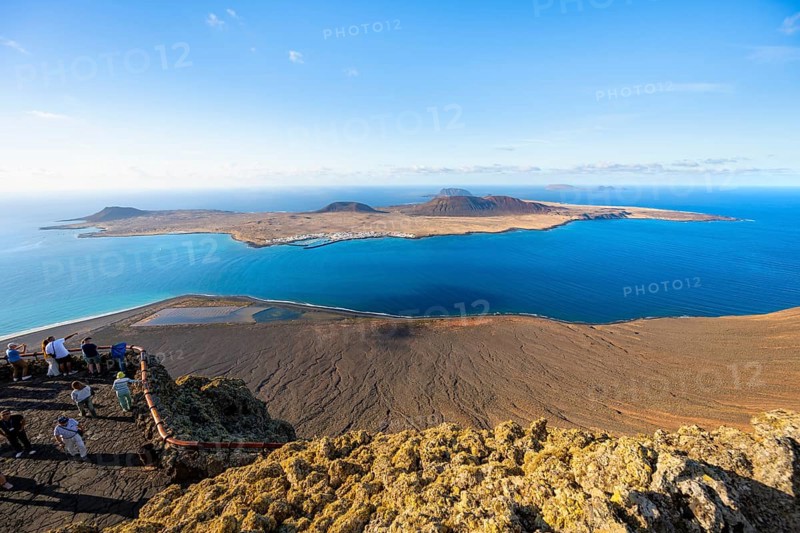 View of La Graciosa island with volcanic craters in the evening light, tourists on an observation deck at the Mirador del Río viewpoint designed by artist César Manrique, Lanzarote, Canary Islands, Spain