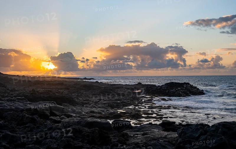 Dramatic cloudy sky with sunbeams at sunset, seaside coast with volcanic rocks, La Santa, Lanzarote, Canary Islands, Spain