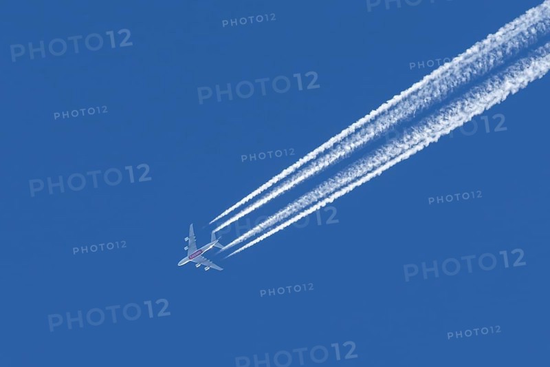 Airbus A380 jet passenger aircraft of Emirates airlines flying in a blue sky with contrails or vapour trails behind, England, United Kingdom