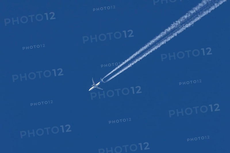 Jet passenger aircraft flying in a blue sky with contrails or vapour trails behind, England, United Kingdom