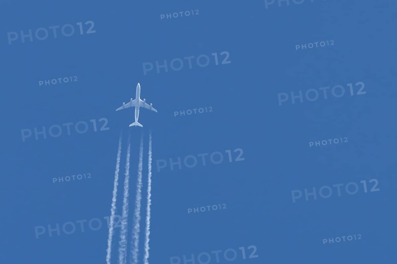 Jet passenger aircraft flying in a blue sky with contrails or vapour trails behind, England, United Kingdom