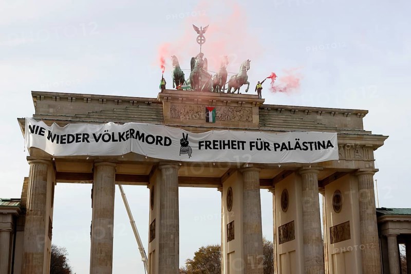 Several activists drop a banner with the inscription Never again genocide, freedom for Palestine and the Palestinian flag and set off pyrotechnics at the Brandenburg Gate, Berlin, 13.11.2025