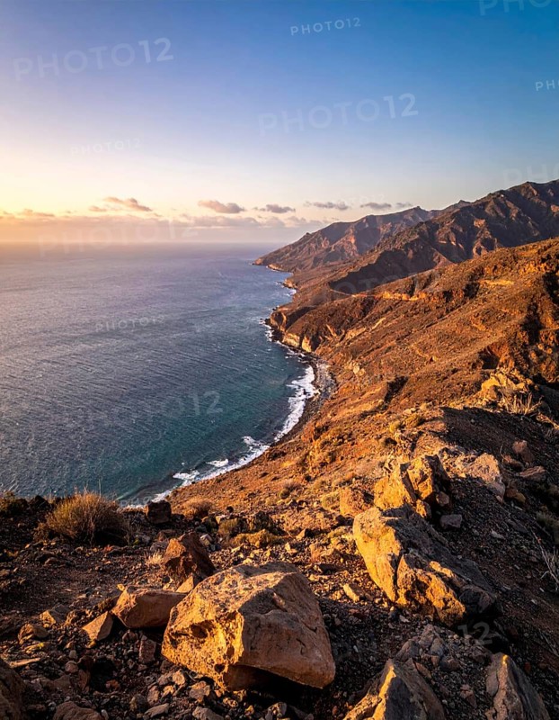 Desert landscape converges with ocean along a rugged coastal area, shore break at cliffs, blue cloudy sky at sunset, dry landscape in an aerial drone view, AI generated