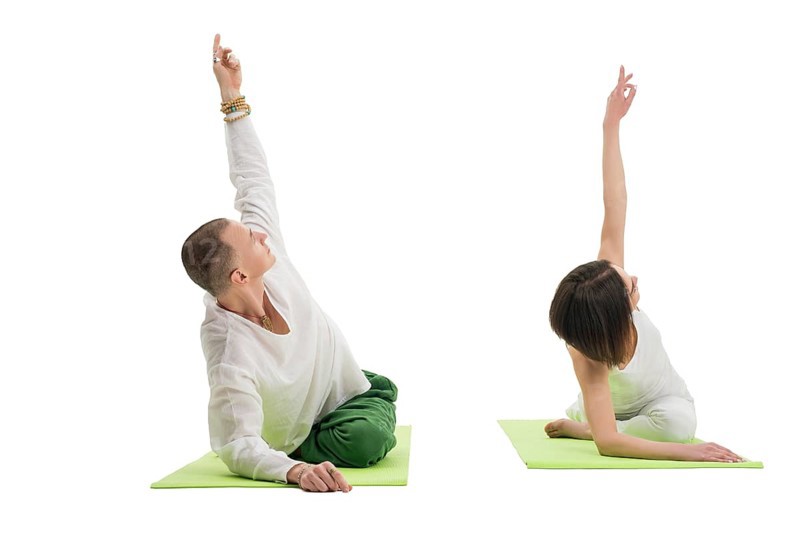 Couple in white sport tshirts and green trousers doing yoga exercises on green mats in studio isolated shot