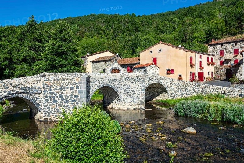Stone bridge over the Pavin couze river flowing through the village of Saurier, Puy de Dome. Auvergne Rhone Alpes, France