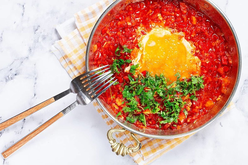 Traditional Turkish dish, scrambled eggs with tomatoes, Menemen, with herbs, in a frying pan, close-up, no people