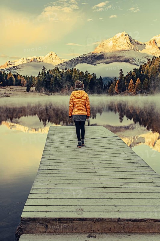 Young woman at Lake Staz near Sankt Moritz in the Engadine in Switzerland. Morning atmosphere with fog in autumn. Reflection of water