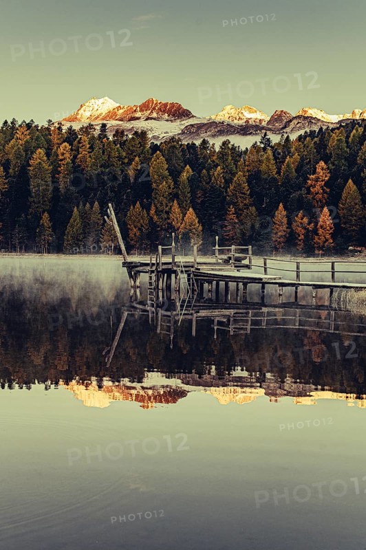 Lake Staz near Sankt Moritz in the Engadin in Switzerland. Morning atmosphere with fog in autumn. Water reflection and snow-covered mountains in the background
