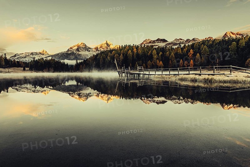 Lake Staz near Sankt Moritz in the Engadin in Switzerland. Morning atmosphere with fog in autumn. Water reflection and snow-covered mountains in the background