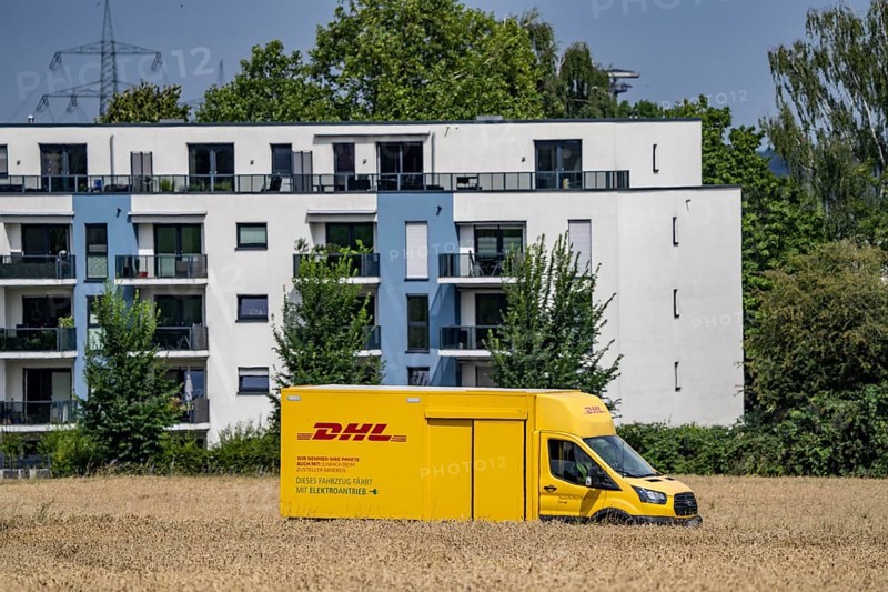 DHL parcel van, electric vehicle, on the way to a customer, rural, driving along a dirt track through a corn field, North Rhine-Westphalia, Germany