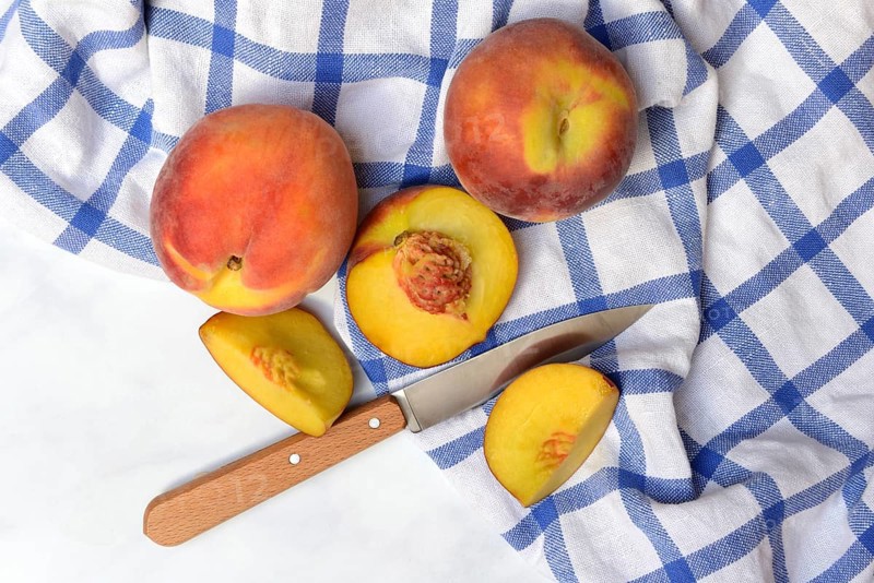 Peach with knife on kitchen towel, peach halves, Prunus persica