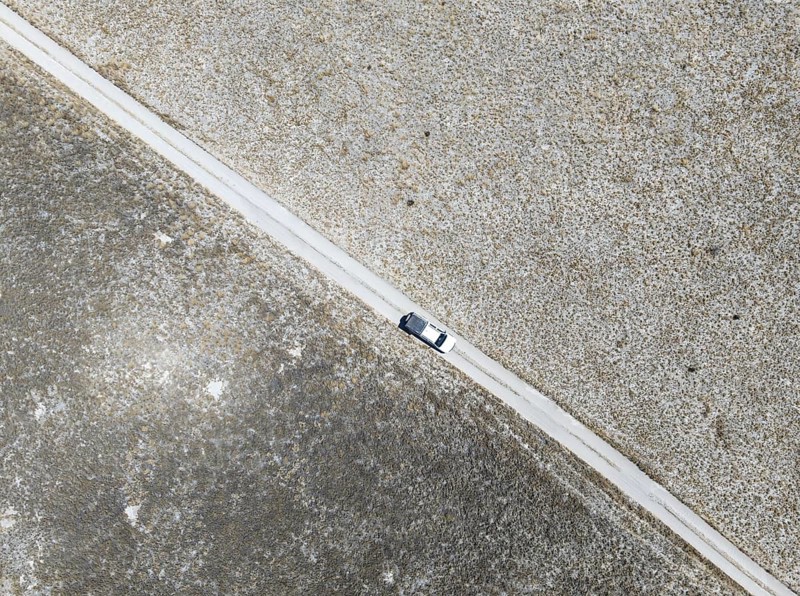 Off-road vehicle driving on a sandy track through a vast dry landscape with yellow grass, Top Down, Sowa Pan, Makgadikgadi salt pans, Botswana