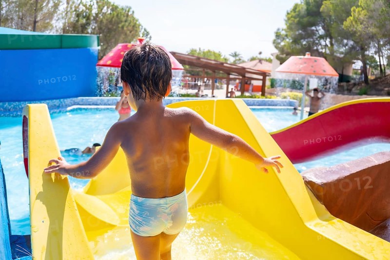 Young boy climbing up a vibrant yellow waterslide at a lively water park, embracing the joy of summer fun and adventure