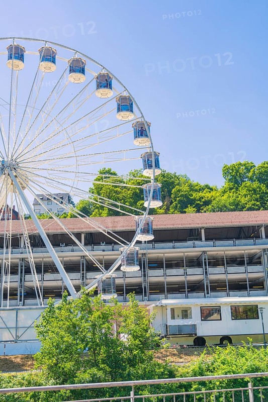 A large Ferris wheel towers over a building, surrounded by green trees under a clear blue sky, 950 years Calw, Germany