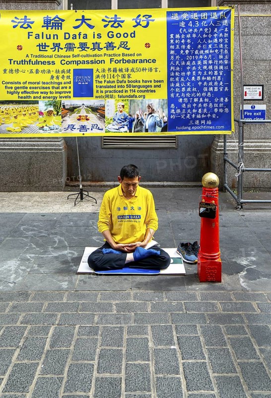 Falun Dafa or Falun Gong man meditating sitting cross legged, Gerrard Street, Chinatown, West End, London, England, UK