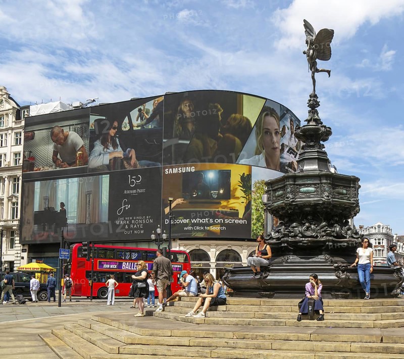 People sitting around Eros statue, Piccadilly Circus, central London, England, UK - Shaftesbury Memorial Fountain