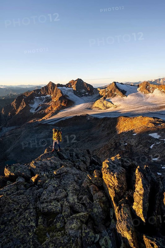 Mountaineers in front of a picturesque high mountain landscape at sunrise with alpenglow, glacier and rocky mountain peaks in the morning light, view at the Becher on mountain peak Königshofspitz and glacier Übeltalferner, Stubai Alps, South Tyrol, Italy