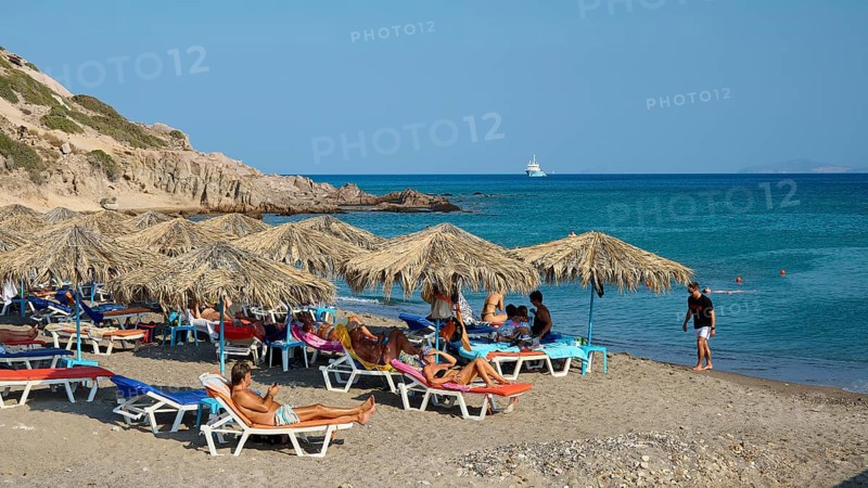 Beach scene with deckchairs and beach mats under umbrellas near the sea, Agios Stefanos Beach, Agios Stefanos Basilica, Chapel of Agios Nikolaos, Kastri Island, Kos, Dodecanese, Greek Islands, Greece