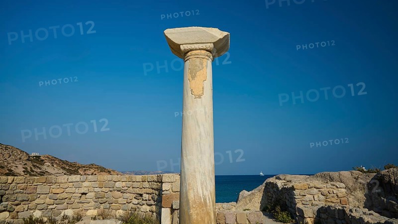 Freestanding stone column in front of a historical site with blue sky in the background, Agios Stefanos Beach, Agios Stefanos Basilica, Chapel of Agios Nikolaos, Kastri Island, Kos, Dodecanese, Greek Islands, Greece