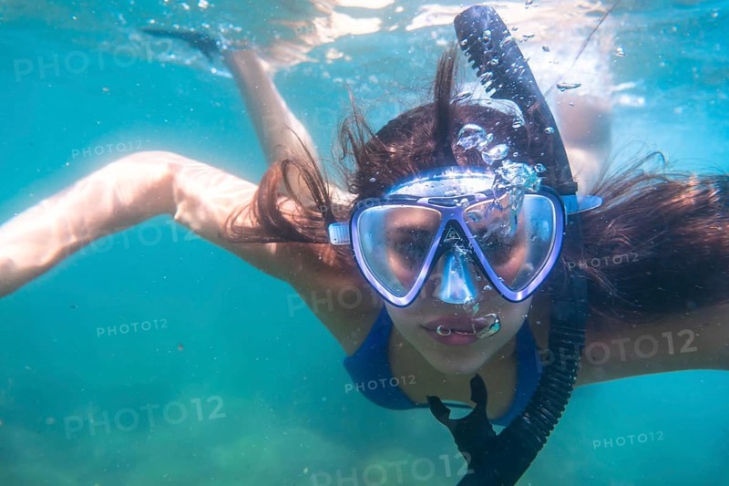 Tourist enjoys snorkeling in crystal clear ocean water, creating a stream of bubbles as she breathes through her snorkel