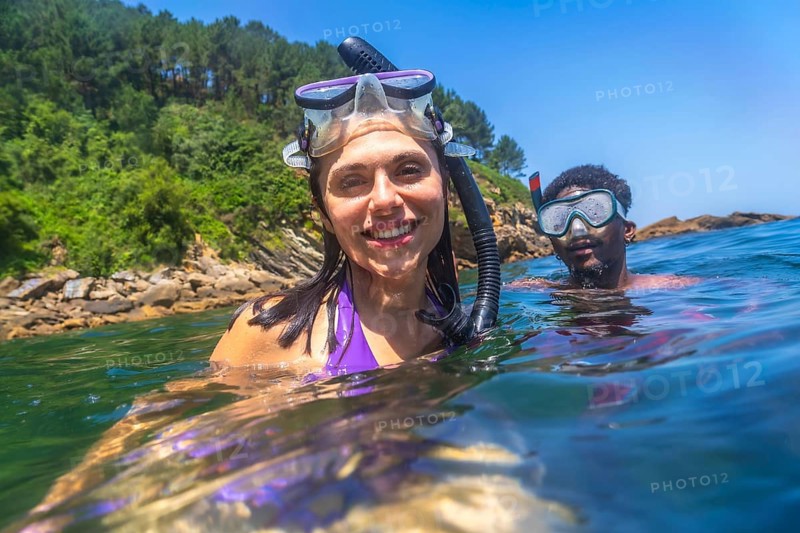 Happy couple snorkeling together in the ocean near the rocky coastline, enjoying their summer vacation