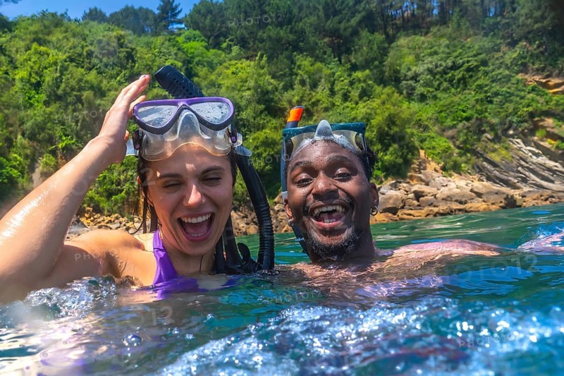 Interracial couple enjoying a fun snorkeling adventure in the vibrant ocean, laughing and sharing joyful moments during a summer vacation
