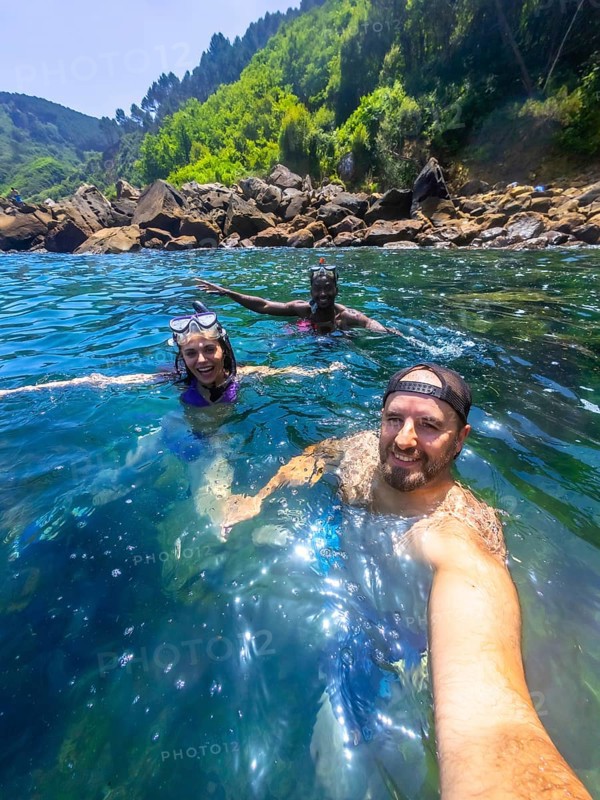 Three friends wearing snorkeling gear and enjoying the refreshing ocean water near a rocky coast